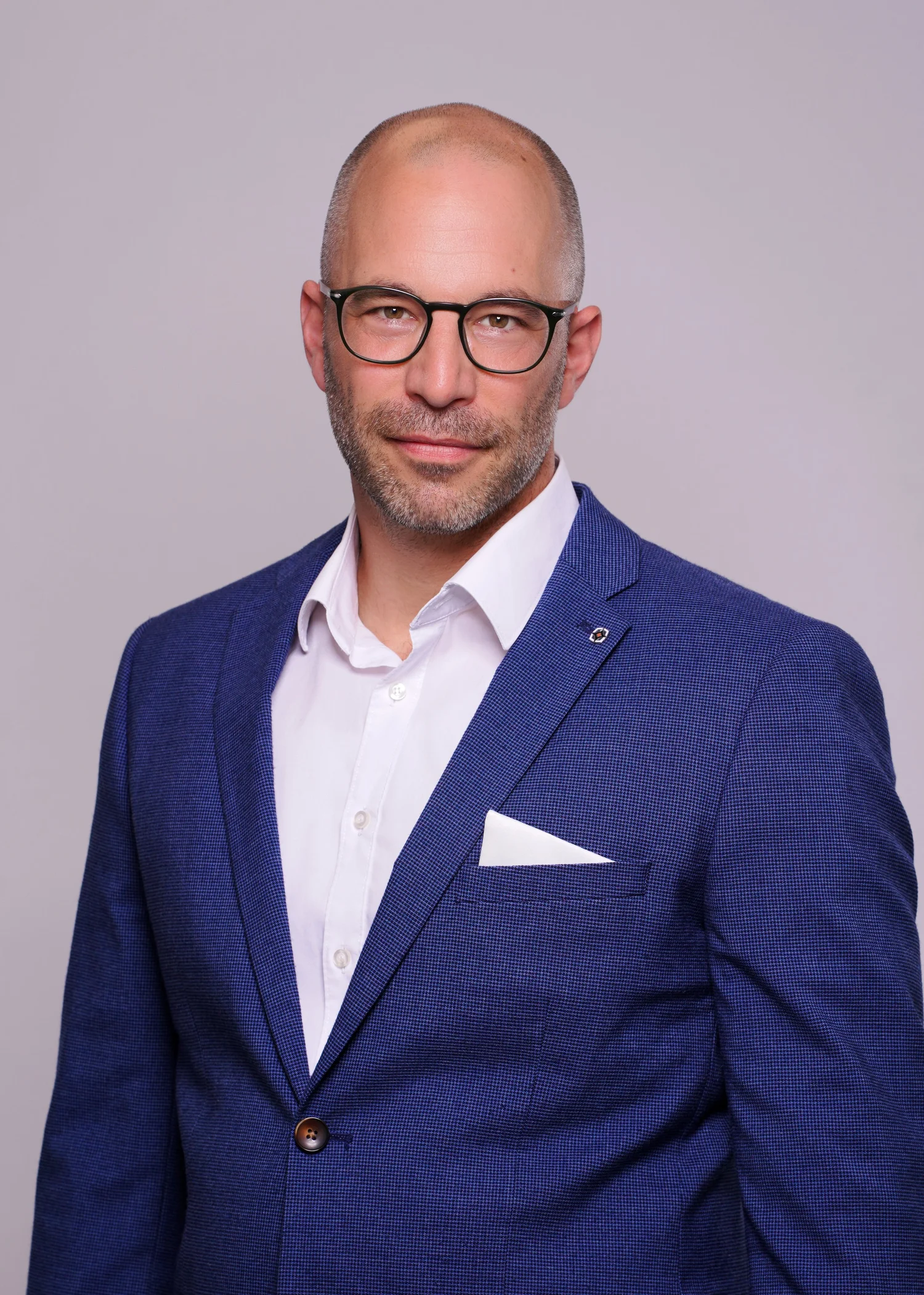 Mann in blauer Anzugjacke mit Brille vor hellem Hintergrund