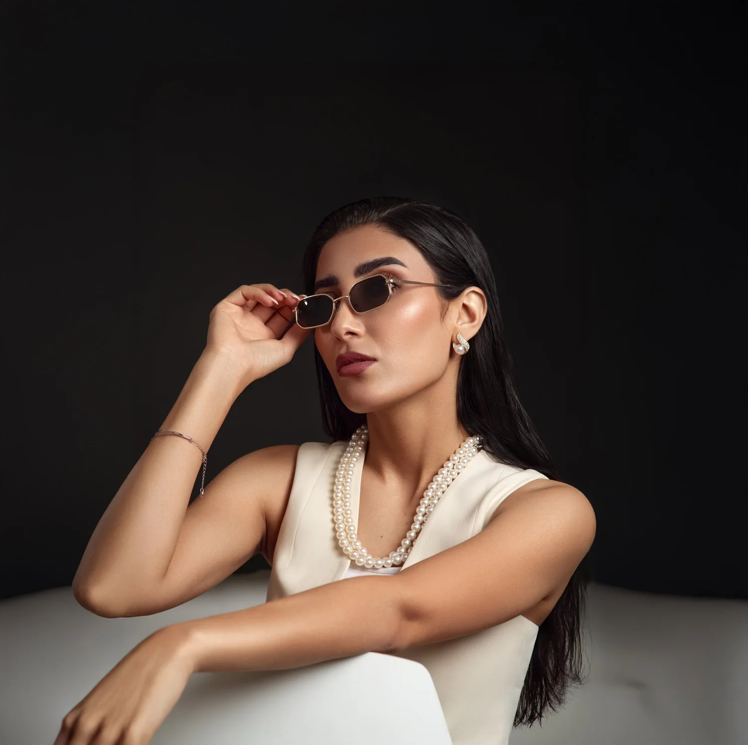 Frau mit dunklem Haar, Sonnenbrille und Perlenkette vor dunklem Hintergrund