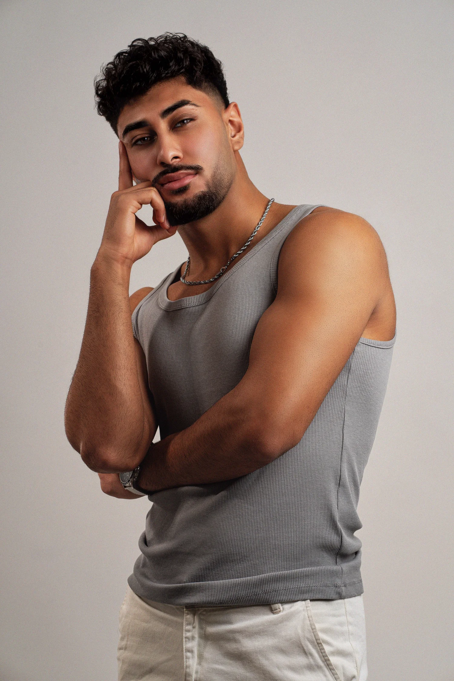 Mann in grauem Tanktop mit Silberkette, nachdenkliche Pose